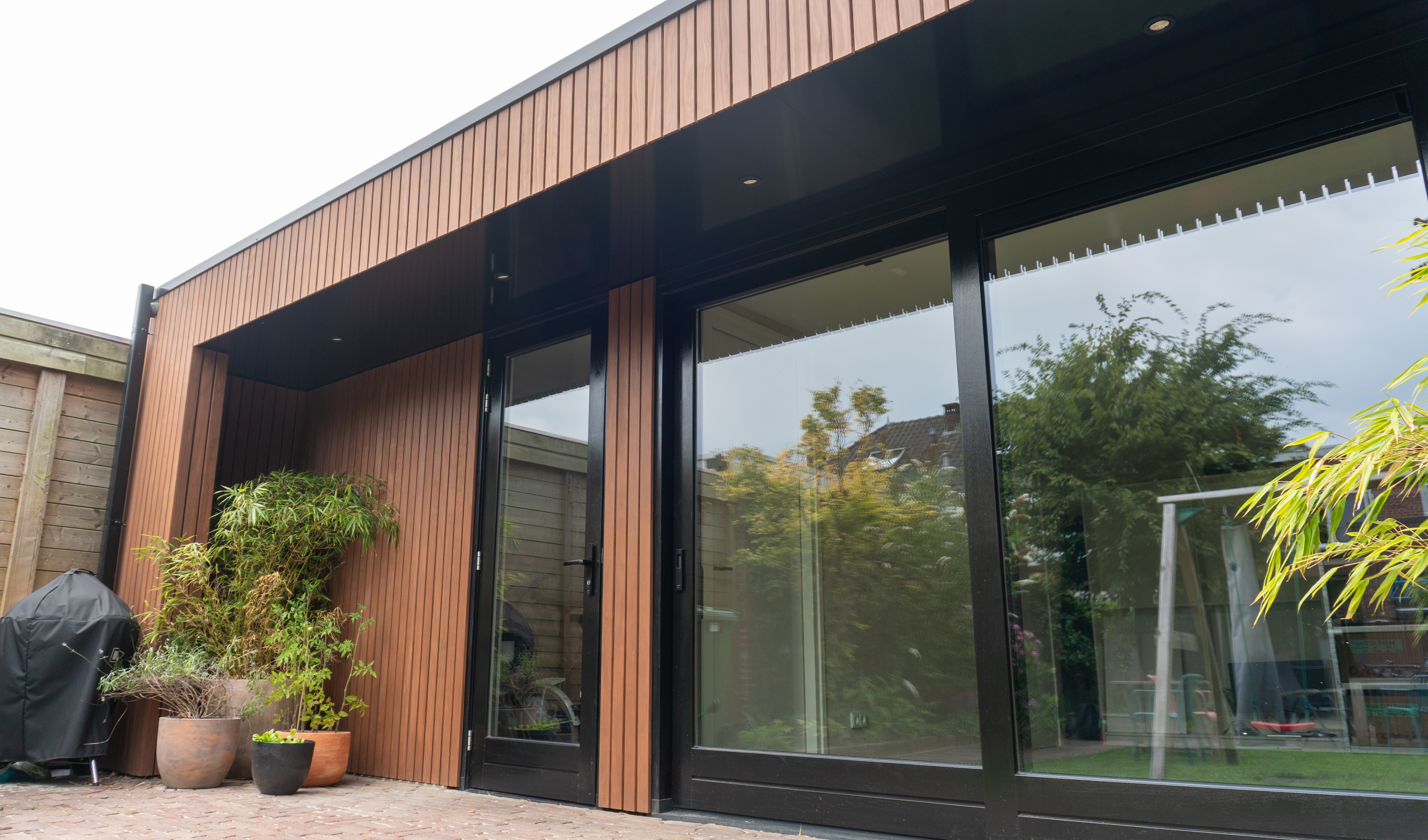 Grote prefab aanbouw met zwarte houten kozijnen.